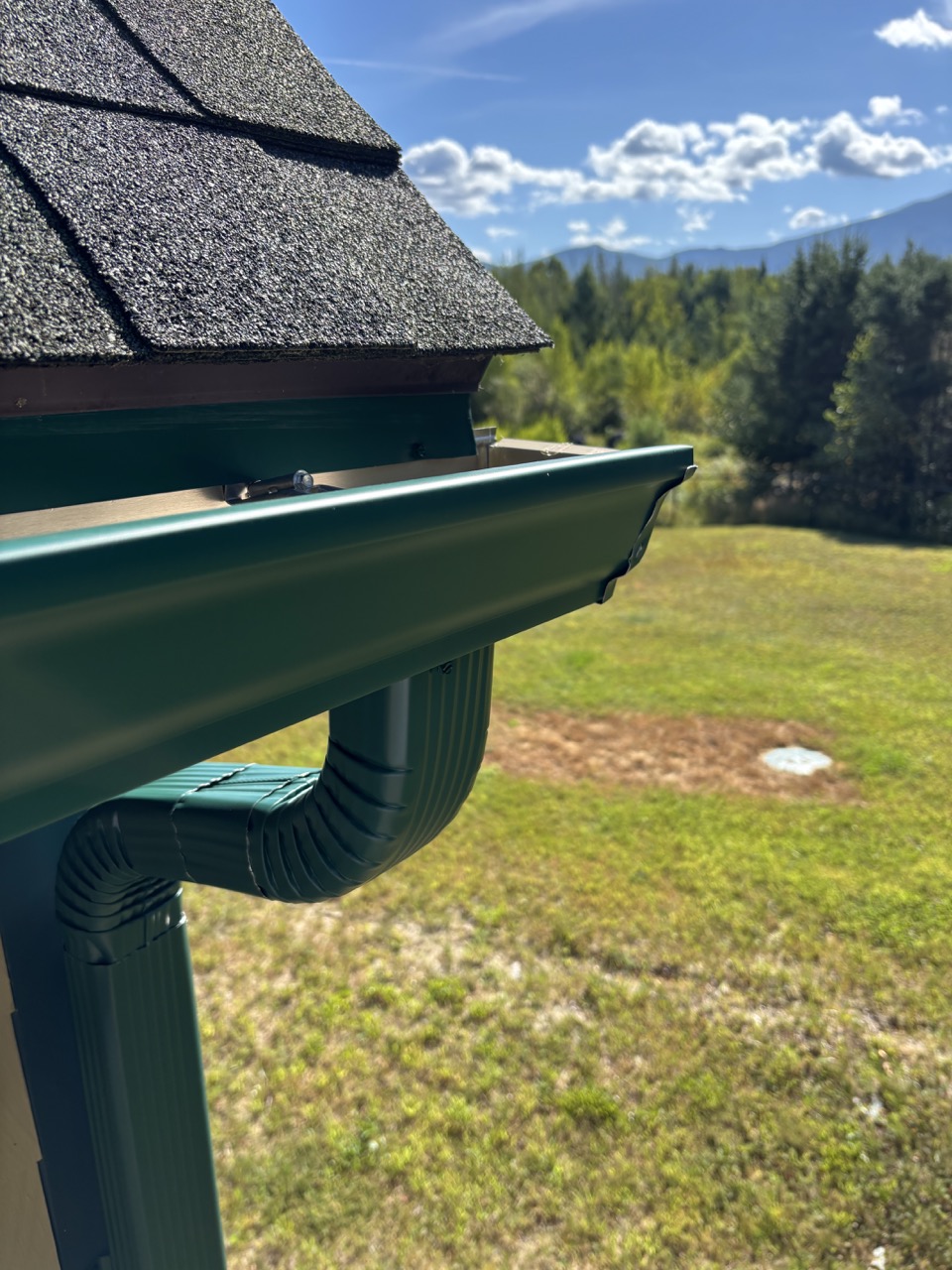 Forest green seamless gutter installation with New Hampshire mountain views